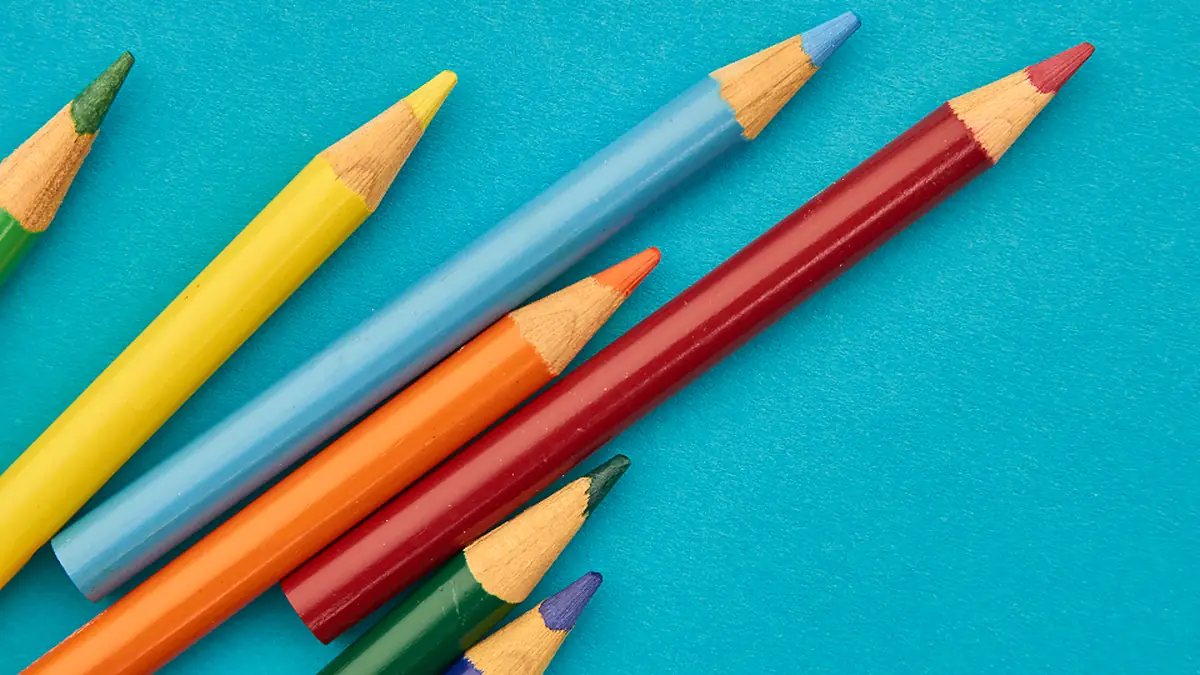 Lápis de cor apontados sobre fundo azul, lembrando material escolar
