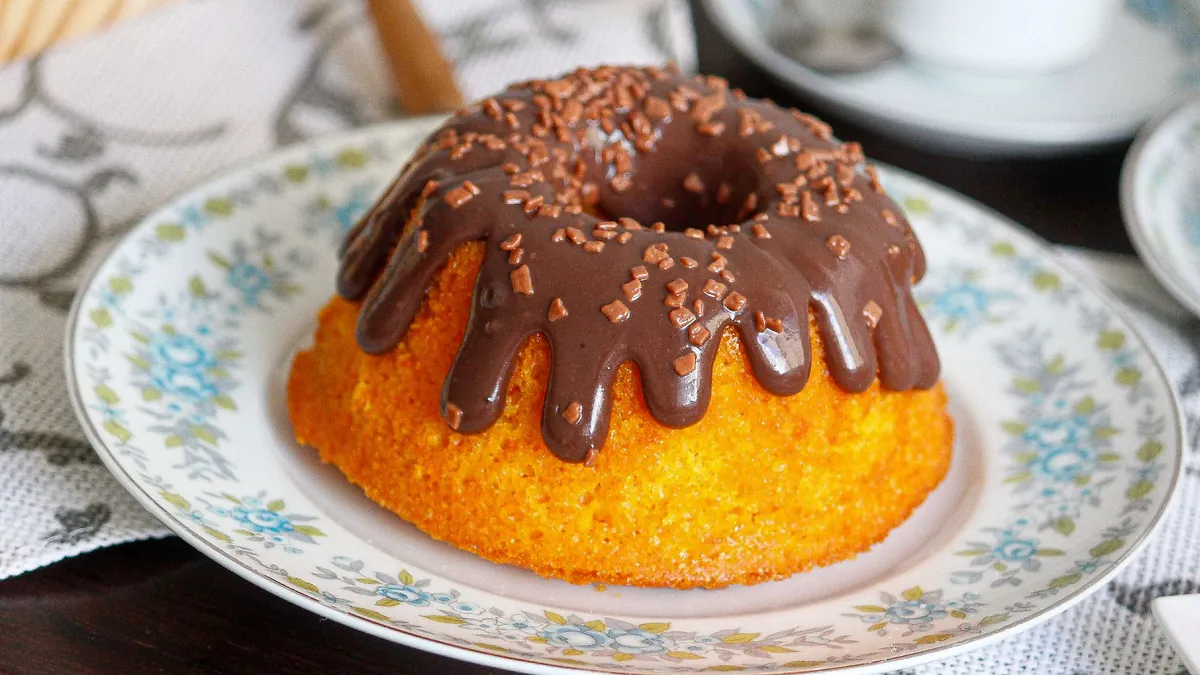 Bolo de cenoura com cobertura de chocolate e granulado, num prato de louça florida