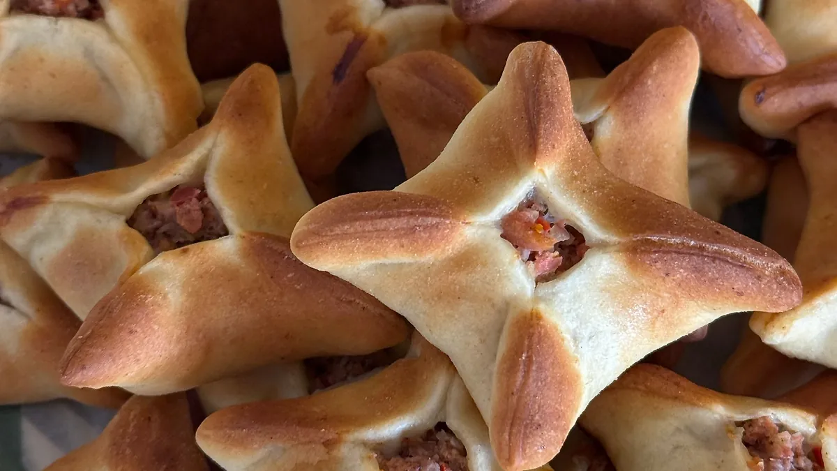Esfirras fechadas assadas, douradas, com recheio de carne aparecendo no meio