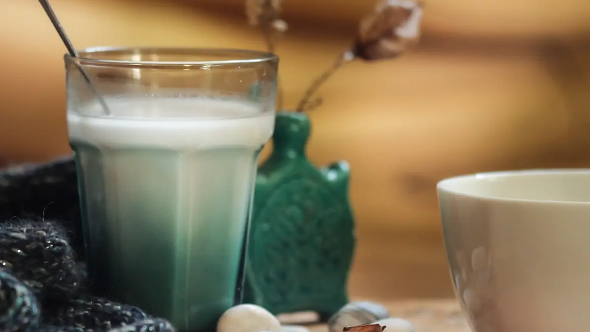 Copo de leite sobre a mesa, ao lado de um vaso e de uma xícara, em luz suave