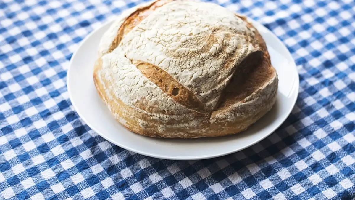 Pão caseiro redondo num prato, sobre toalha xadrez azul