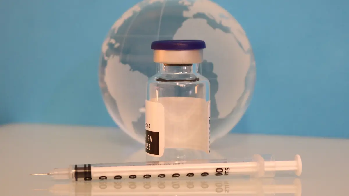 Frasco de vacina e seringa sobre uma mesa clara, com um globo de vidro ao fundo azul
